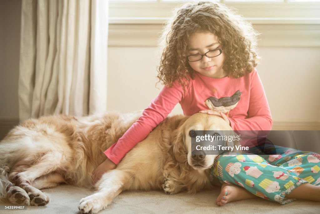 Mixed race girl petting dog on floor