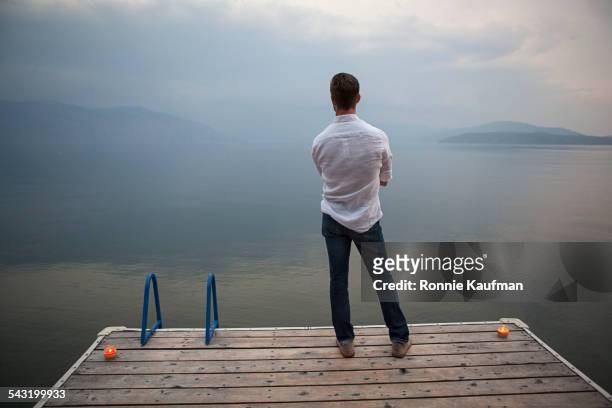 caucasian man standing on wooden dock over lake - rückansicht stock-fotos und bilder