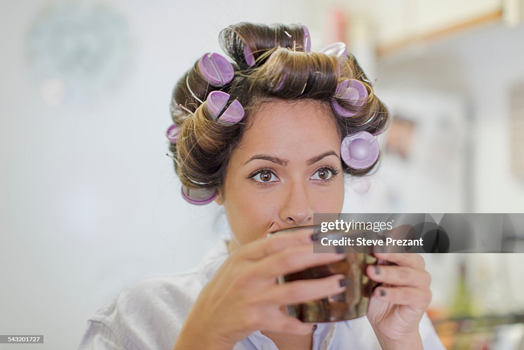 Close up of mid adult woman wearing hair rollers drinking coffee