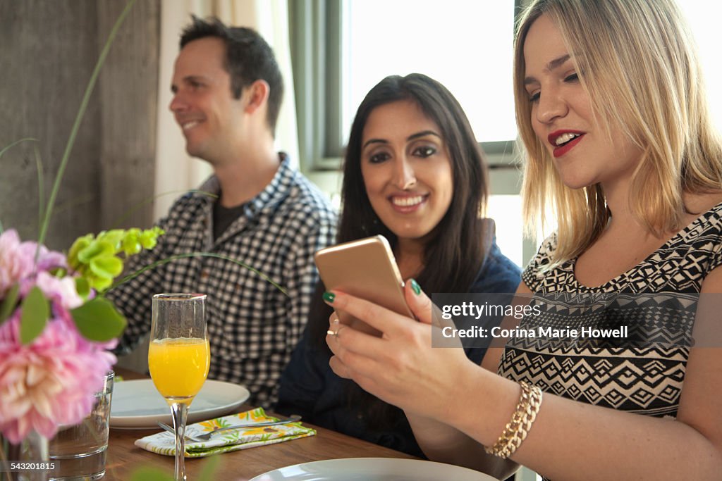 Friends at dinner table, young woman showing friend smartphone screen