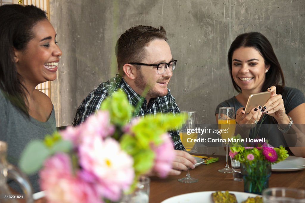 Friends at dinner table, young woman showing friend smartphone screen