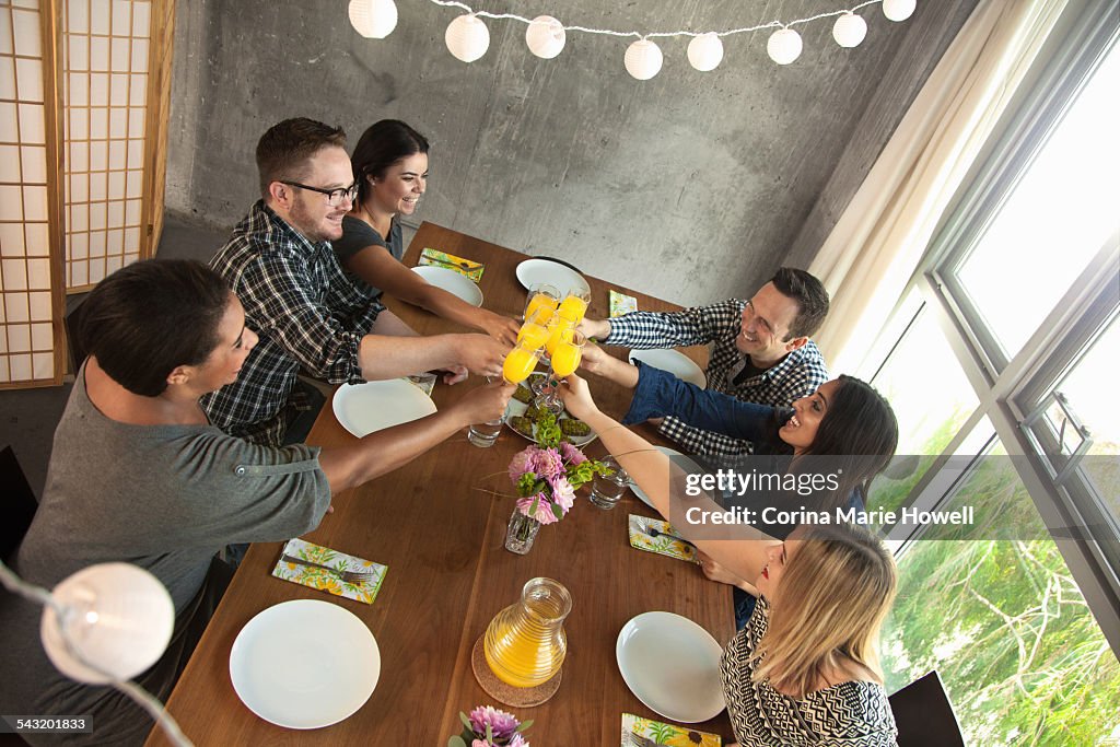 Group of friends around table, raising glasses, making toast