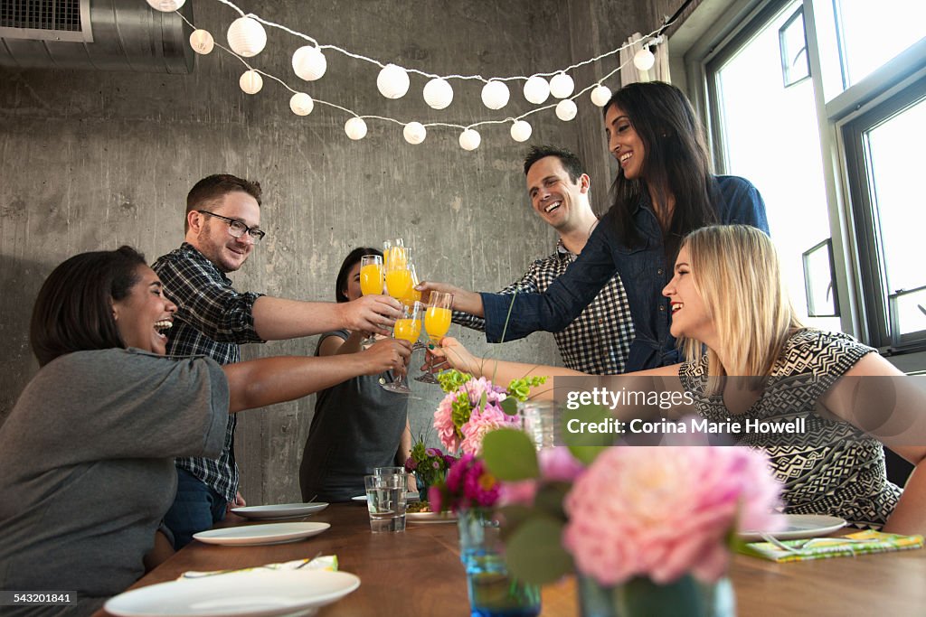 Group of friends around table, raising glasses, making toast