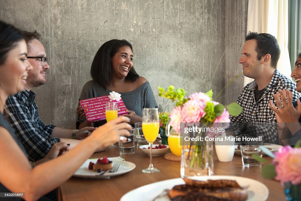 Group of friends at dinner table, Young woman holding wrapped gift