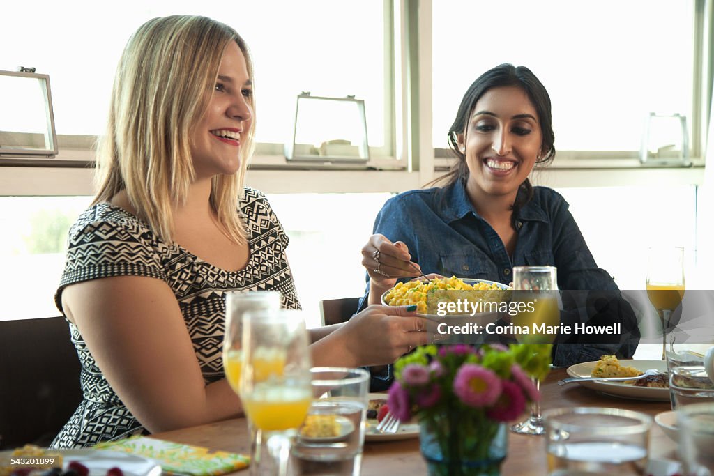 Group of friends having meal at table, young woman passing plate to friend