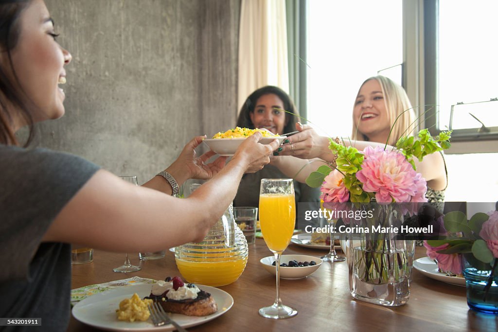 Group of friends having meal at table, young woman passing plate to friend