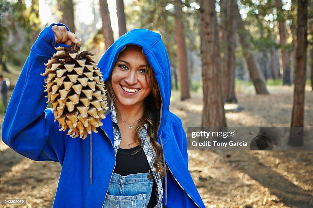 Portrait of young woman in forest holding up large pine cone, Los Angeles, California, USA
