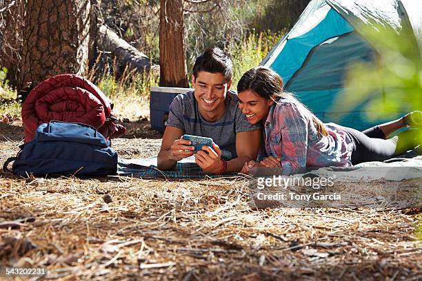 young camping couple looking at smartphone in forest, los angeles, california, usa - allongé sur le devant photos et images de collection