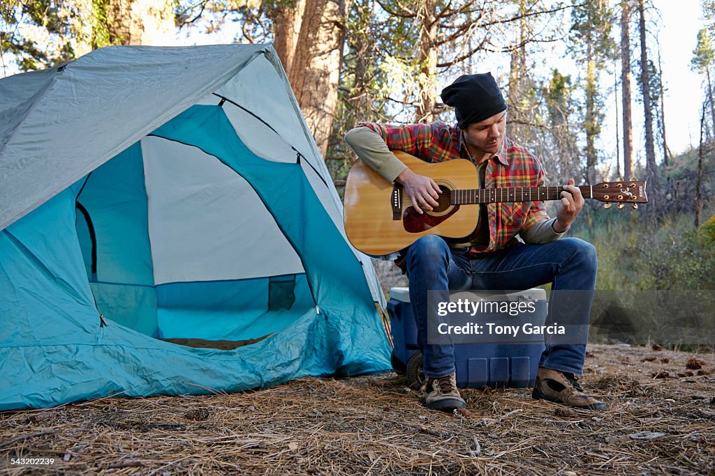 Young male camper playing guitar in forest, Los Angeles, California, USA