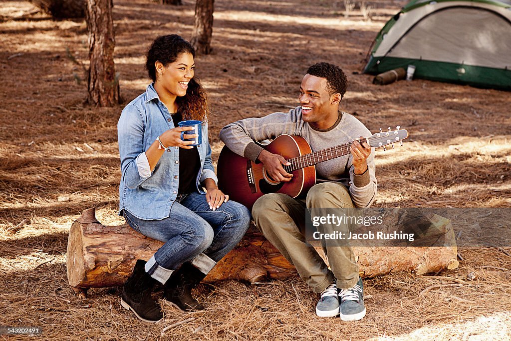 Young couple sitting on forest log playing acoustic guitar