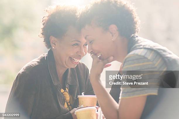 two mature female friends laughing whilst drinking takeaway coffee on street - ハイキー 街 ストックフォトと画像