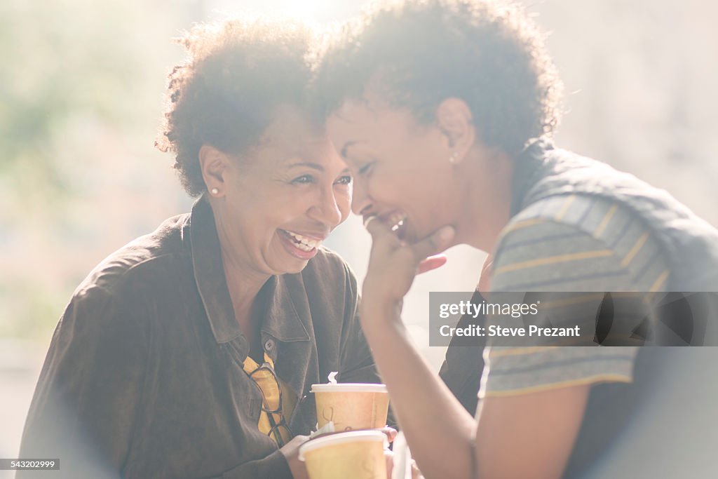 Two mature female friends laughing whilst drinking takeaway coffee on street