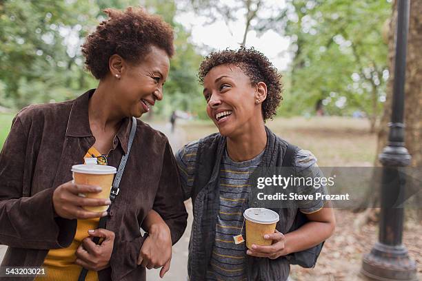 two mature female friends drinking takeaway coffee whilst strolling in park - african american couple walking park ��ストックフォトと画像