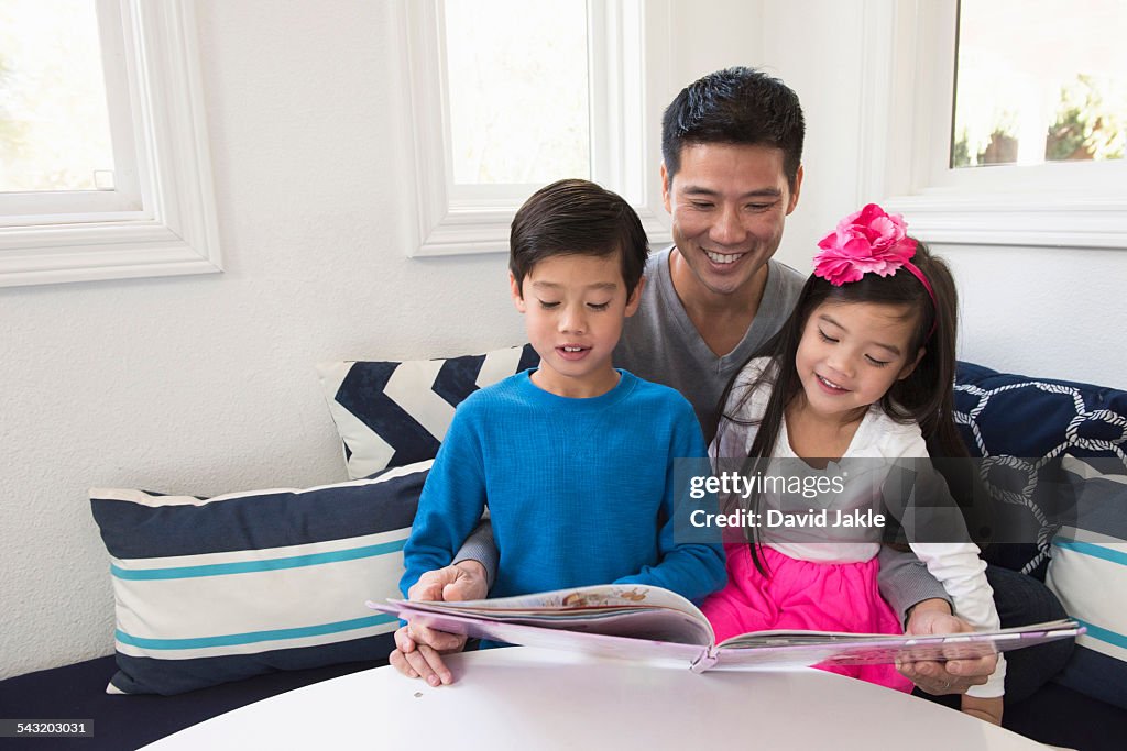 Mature man reading storybook to son and daughter on sofa