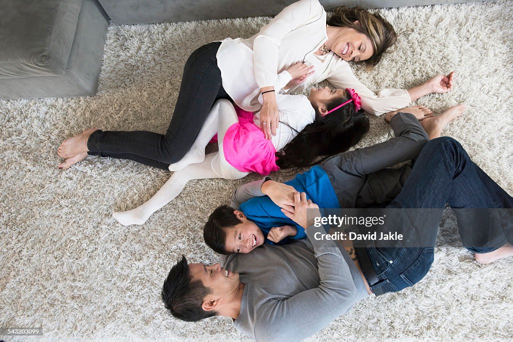 Overhead view of mature couple and two children play fighting on living room floor