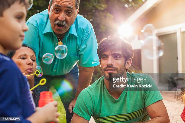 three generation family blowing bubbles in garden - older woman bending over stock pictures, royalty-free photos & images