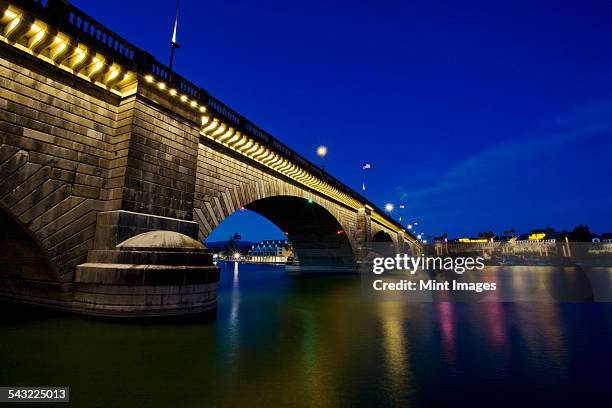 london bridge at night, spanning the waters of lake havasu. reflections in calm water.  - london bridge arizona stockfoto's en -beelden