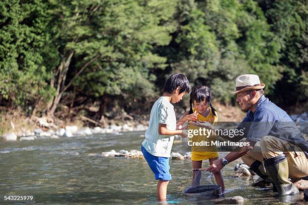 father and two children playing by a river. - asian smiling father son stock pictures, royalty-free photos & images