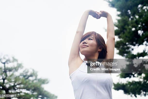 a woman in a kyoto park, wearing headphones. wearing jogging kit and stretching before exercise. - sleeveless shirt stock pictures, royalty-free photos & images