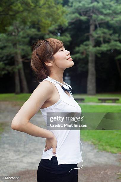 a woman in a kyoto park, wearing headphones. wearing jogging kit and stretching before exercise. - sleeveless stock pictures, royalty-free photos & images