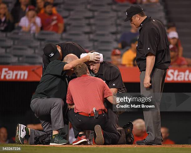 Umpire Paul Emmel is treated by athletic trainers Walt Horn of the Oakland Athletics and Adam Nevala of the Los Angeles Angels of Anaheim after being...