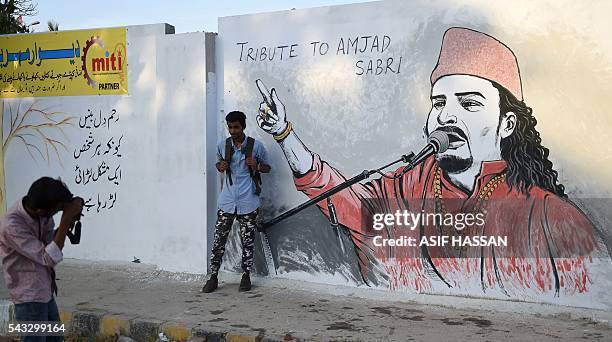 Pakistani student takes a photograph of his friend next to a wall image of late Sufi musician Amjad Sabri in Karachi on June 27, 2016. One of...