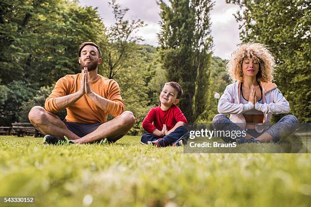 jeune souriant famille faisant du yoga exercices de détente sur une herbe. - family yoga photos et images de collection