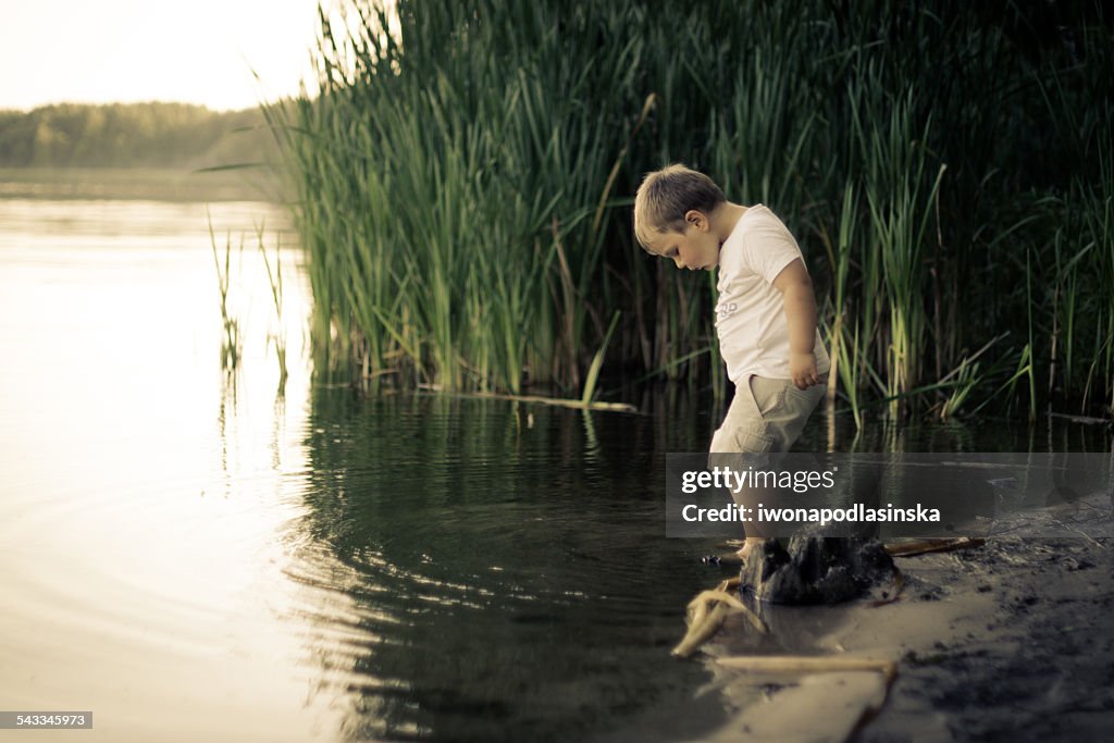 Portrait of boy testing the water of calm pond with leg