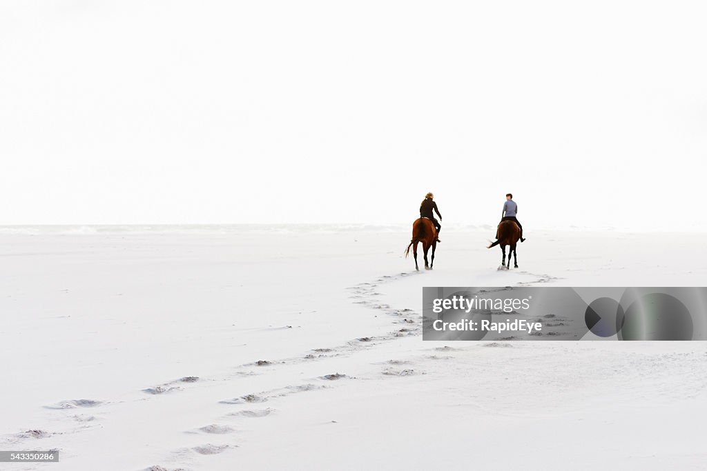 Two horseriders leave hoofprints in the sand on winter day