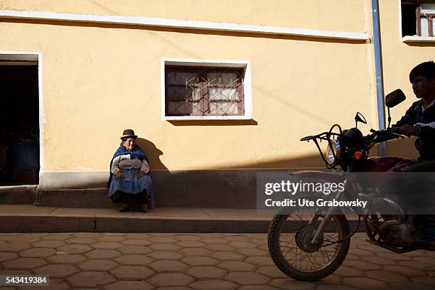 Bolivar, Bolivia An old woman is sitting in front of a house in a small village in the Andes. In the foreground, a motorcycle passes on April 14,...