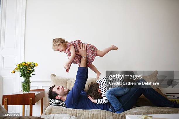 a dad playing with his children on a sofa - family on couch stock pictures, royalty-free photos & images