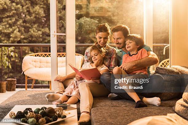 felizes pais uma ler um livro com sua pequena criança. - family home imagens e fotografias de stock