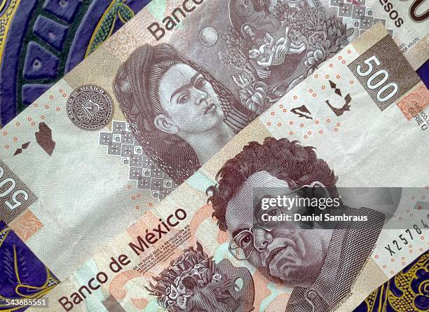 Mexican pesos notes on a table with traditional Mexican ornament. The note has the portrait of the painter Diego Riviera on one side and Frida Kahlo...