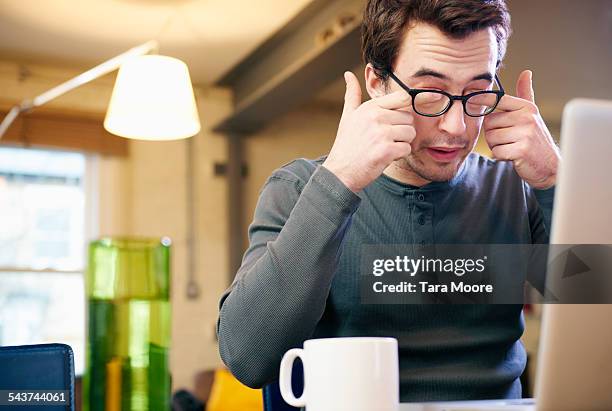 young man with laptop at home rubbing his eyes - rubbing eyes stock pictures, royalty-free photos & images