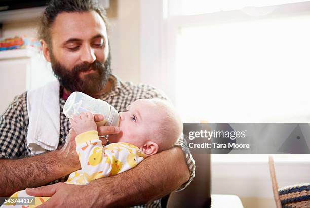 father feeding baby in arm with bottle at home - lean in collection father stock-fotos und bilder