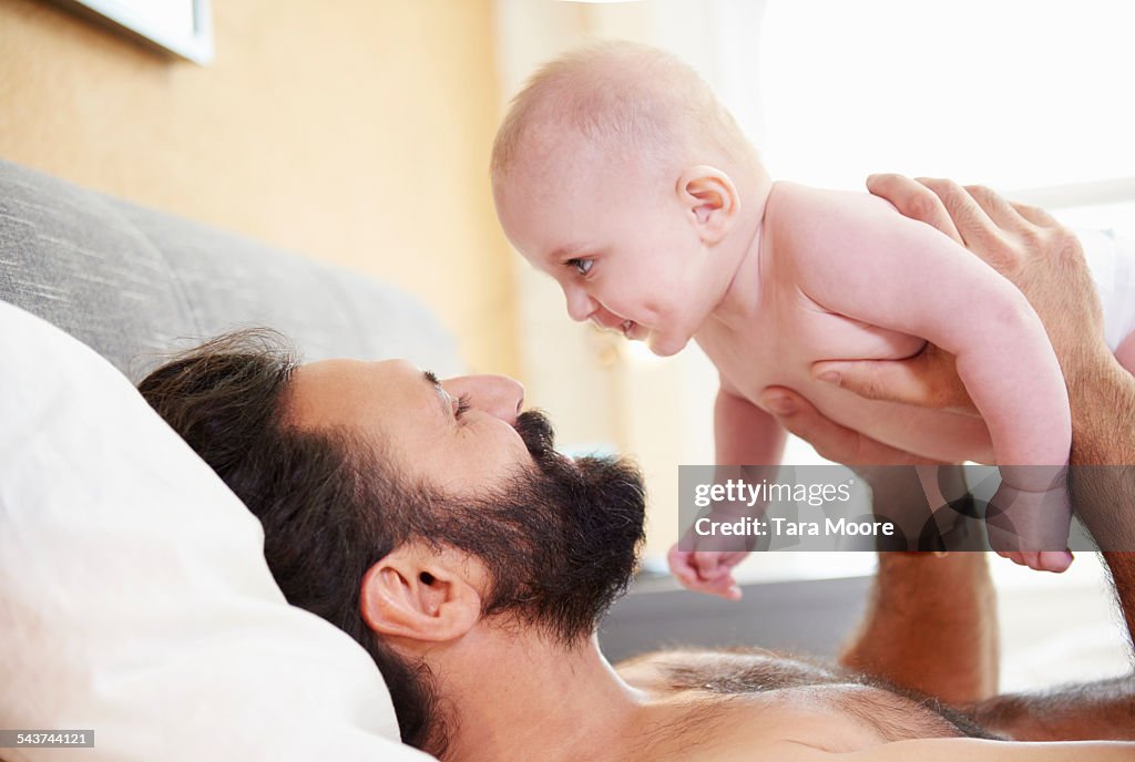 Father holding baby lying in bed at home