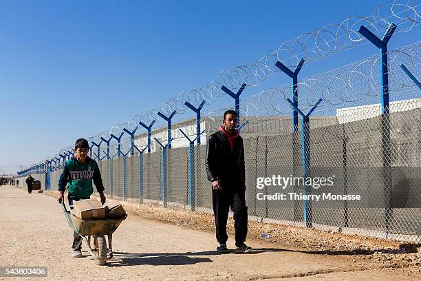 Za'atari, Mafraq Governorate, Jordan, February 5; 2014. -- A man and a child who push a Wheelbarrow walk beside a school surounded by barbed wire in...