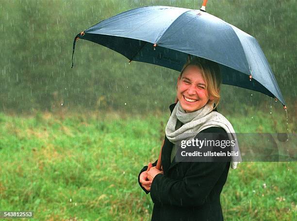 Lächelnde junge Frau mit Regenschirm bei einem Spaziergang. Regenwetter; Nieselwetter; Schmuddelwetter. .