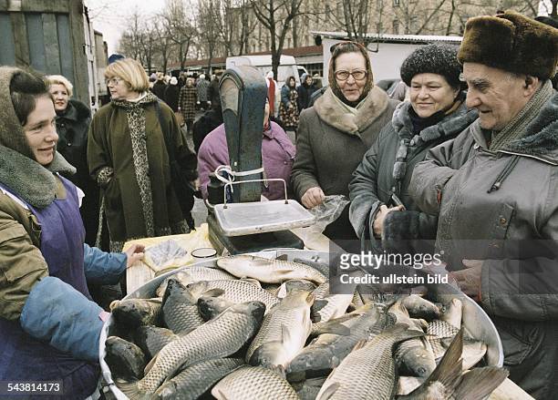 Auf einem Markt in Kiew, Ukraine, stehen mehrere Menschen, Männer wie Frauen, um einen Fischstand. Eine Fischverkäuferin bietet frischen Fisch an,...
