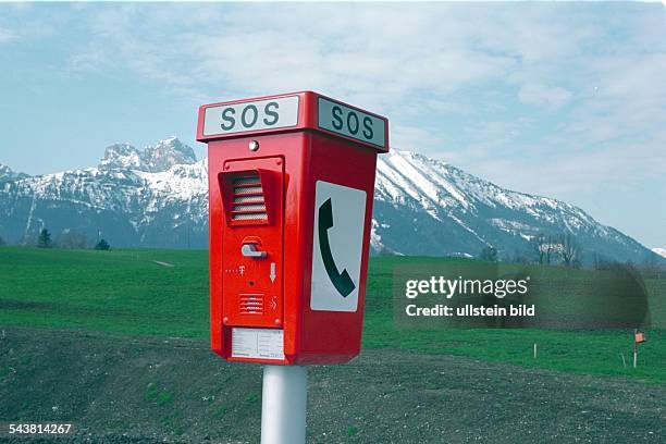 Säule der Telekom an einer Straße bei Pfronten im Allgäu. Im Hintergrund ein schneebedeckter Berg. Piktogramm; Telefonhörer; Notruf; einsame Gegend. .