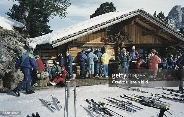 Die Holzhütte, genannt "Eierlikörhütte", im Skigebiet Plan de Gralba in Südtirol. Skiläufer rasten draußen bei Sonnenschein, holen sich am Tresen der...