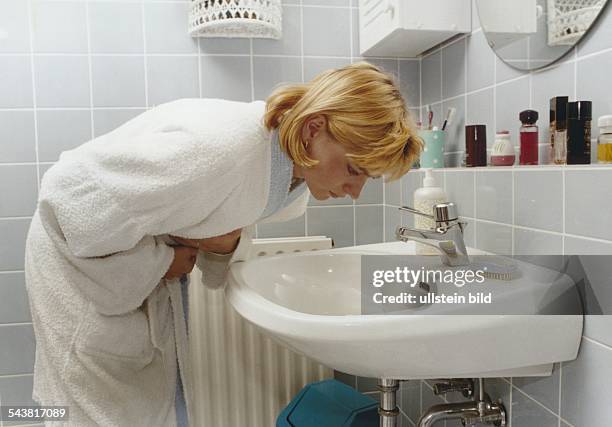 Eine Frau krümmt sich vor Schmerzen über ein Waschbecken im Badezimmer. Magenschmerzen; Bauchschmerzen; Übelkeit. Symbolbild Aufgenommen Oktober 1994.