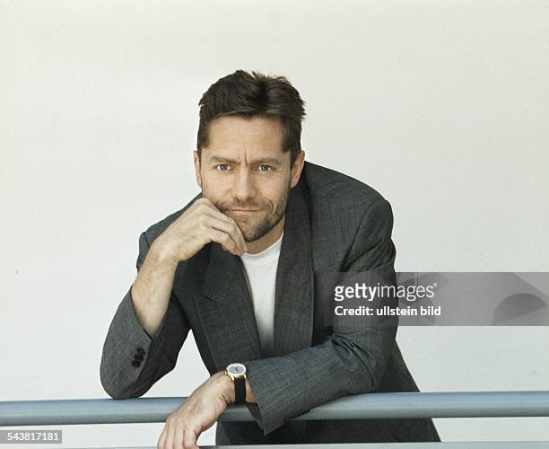 Der Schauspieler Udo Schenk lehnt an einem Geländer. Er trägt eine graue Jacke mit weißem T-Shirt, am Handgelenk eine Armbanduhr. Aufgenommen August...