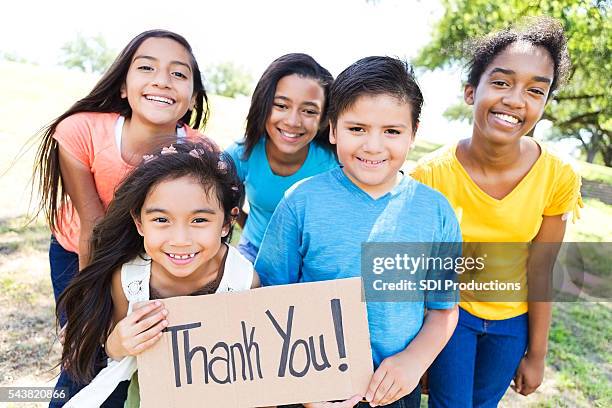 young diverse friends in local park hold 'thank you!' sign - kids smiling multiple nationalities stock pictures, royalty-free photos & images