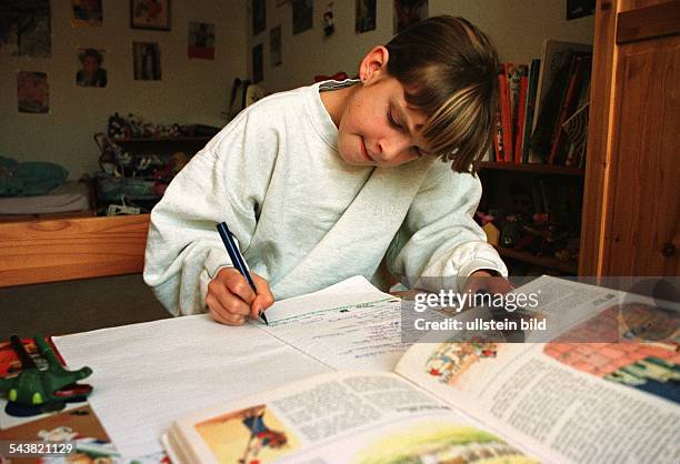 Ein Mädchen sitzt in ihrem Kinderzimmer am Schreibtisch und schreibt mit einem Füller in ein Schulheft. Vor ihr liegt ein aufgeschlagenes Schulbuch....