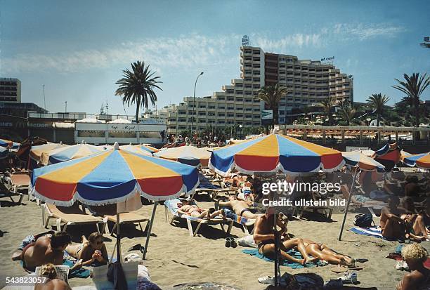 Playa del Ingles / Kanarische Inseln: Touristen / Menschen unter Sonnenschirmen am Strand. Im Hintergrund Restaurants und Hotels. Tourismus;...