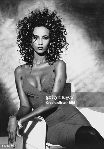 Das Fotomodell Iman sitzt in einem dekolletierten Kleid auf einem Sessel. Aufgenommen um 1992.