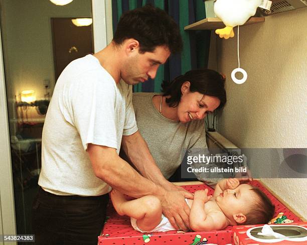 Familie: Der Vater legt seinem Kind eine neue Windel an, während die Mutter nebem dem Wickeltisch steht. Säugling. .