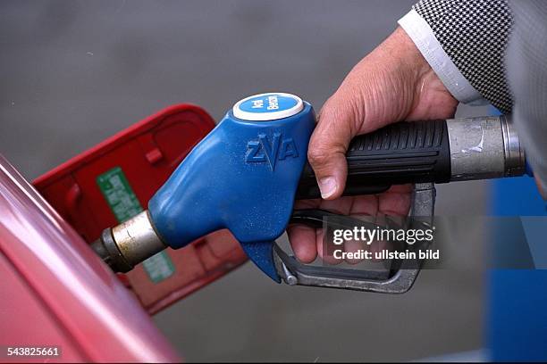 Ein Mann hält an einer Tankstelle den Zapfhahn einer Zapfpistole in den Benzintank seines Pkws. Aral; Benzin; Kraftstoff; Tankdeckel; Tankstellen .