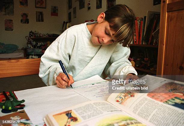 Ein Mädchen sitzt in ihrem Kinderzimmer an einem Schreibtisch, vor sich ein aufgeschlagenes bebildertes Buch, und schreibt in ein Schulheft. Bildung;...